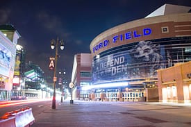 Night view of a brightly lit basketball arena with fans outside.